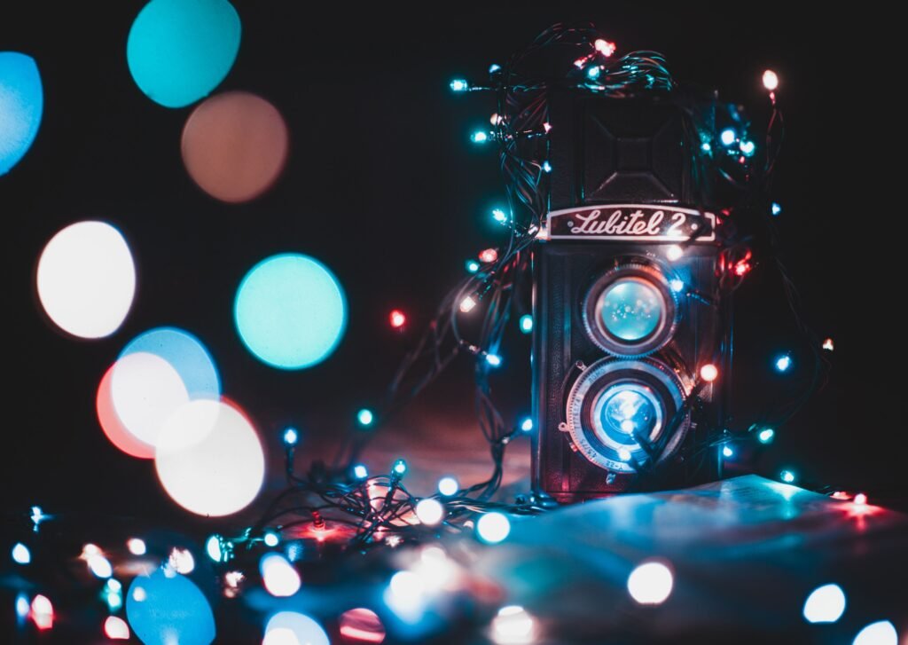 A vintage Lubitel 2 twin-lens camera wrapped in string lights, surrounded by large out-of-focus bokeh circles in blue, teal, and warm tones.